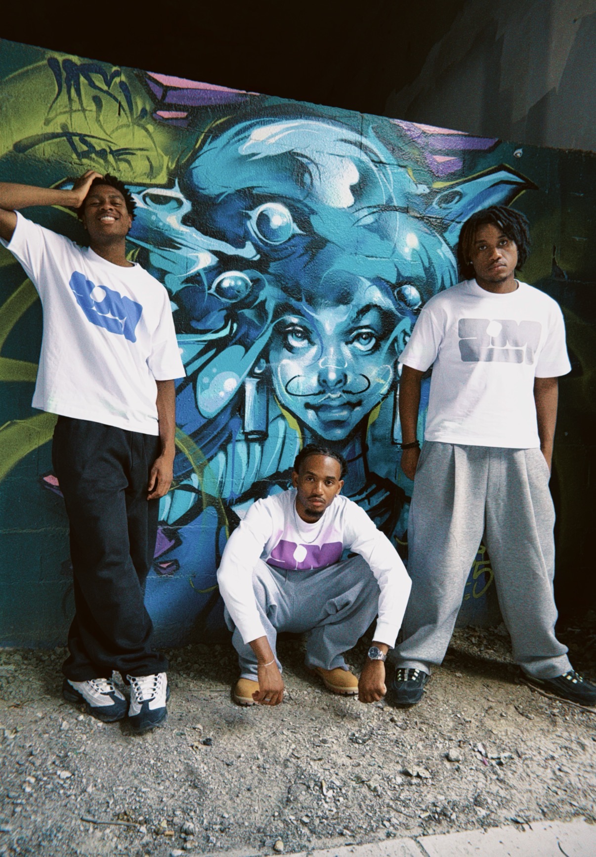 Trois silhouettes ZHOMMES devant une fresque bleue