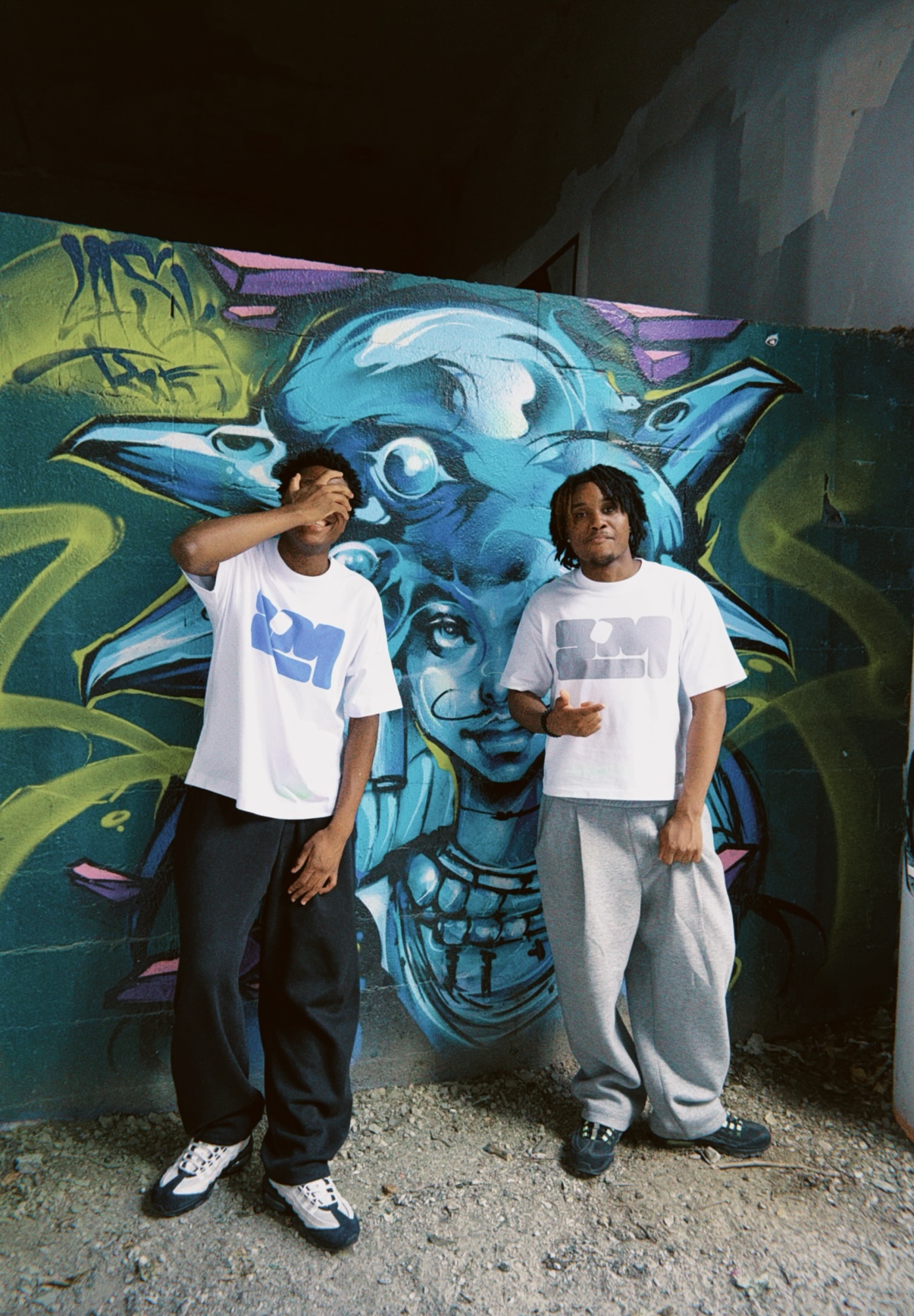 Deux silhouettes ZHOMMES devant une fresque bleue